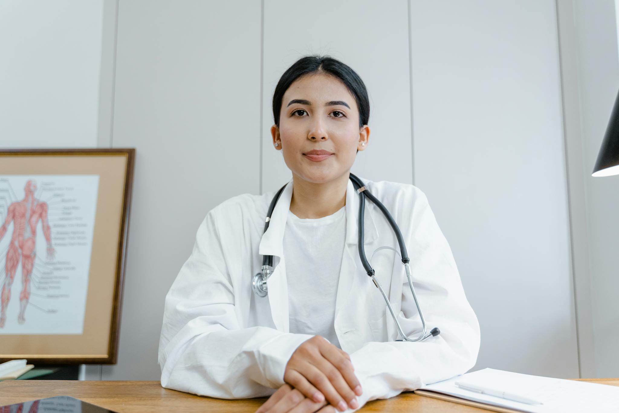 A female doctor confidently sits at her desk, ready for consultation in a medical office.