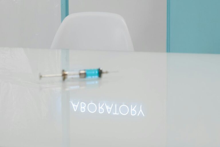 A syringe on a glass table with a laboratory reflection in a clean, clinical setting.