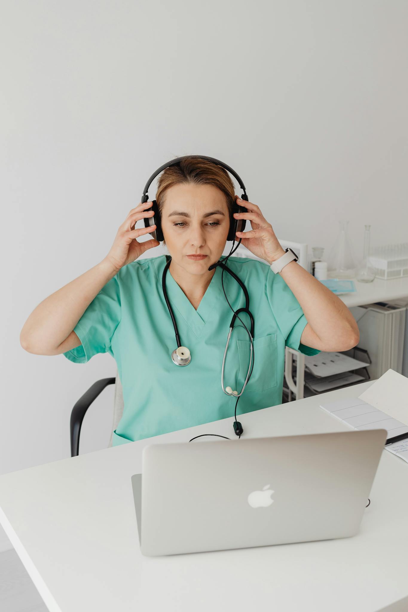 Female doctor in scrubs with stethoscope using a laptop for an online medical consultation.